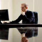 Man in business attire shopping for glasses online at a desktop computer in an office